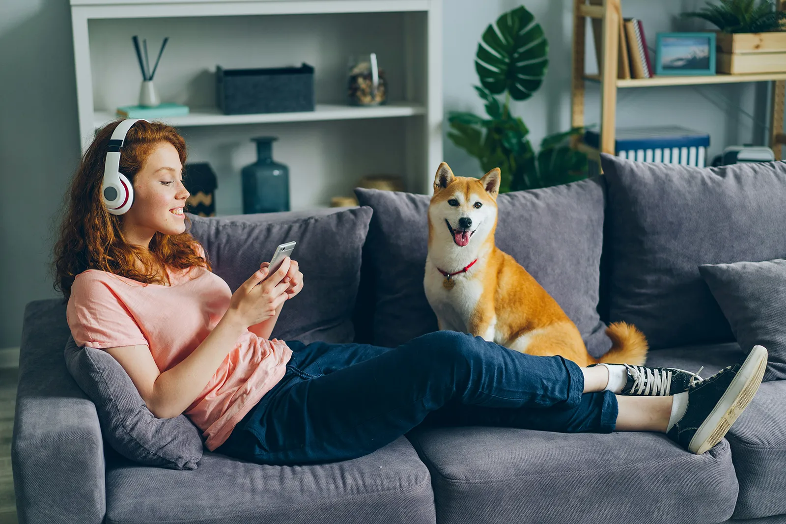 A woman online shopping while listening to music laying on the sofa with her dog