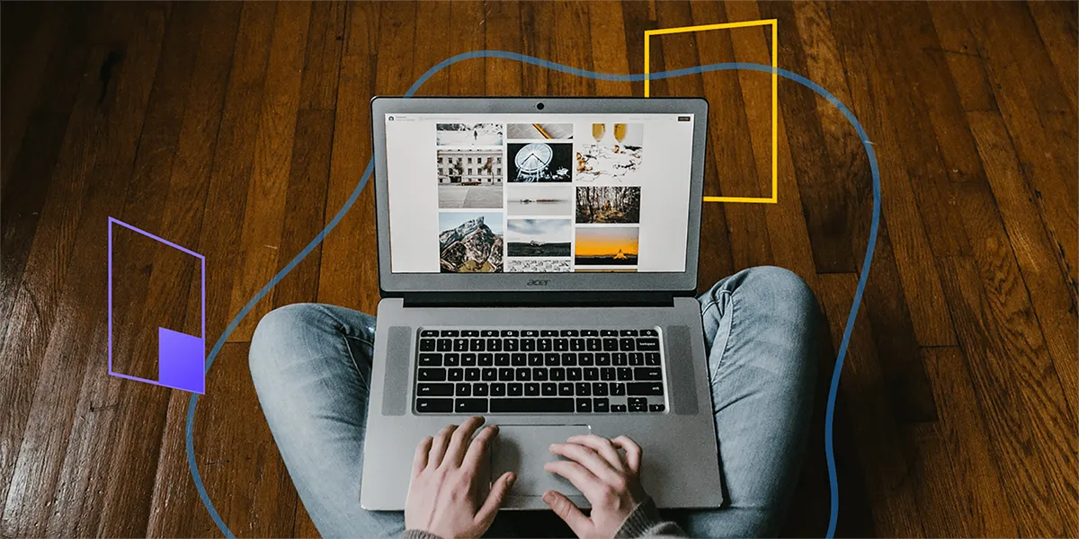 A man sat on a wooden floor looking at images on a laptop