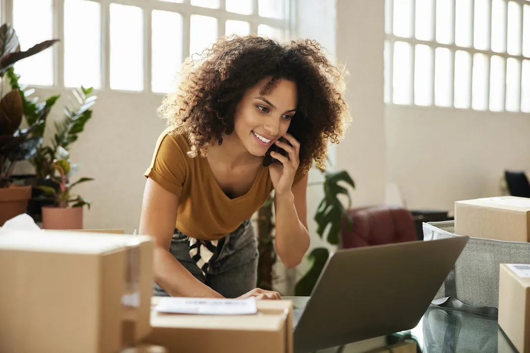 A woman on the phone while packing up orders for her e-commerce business