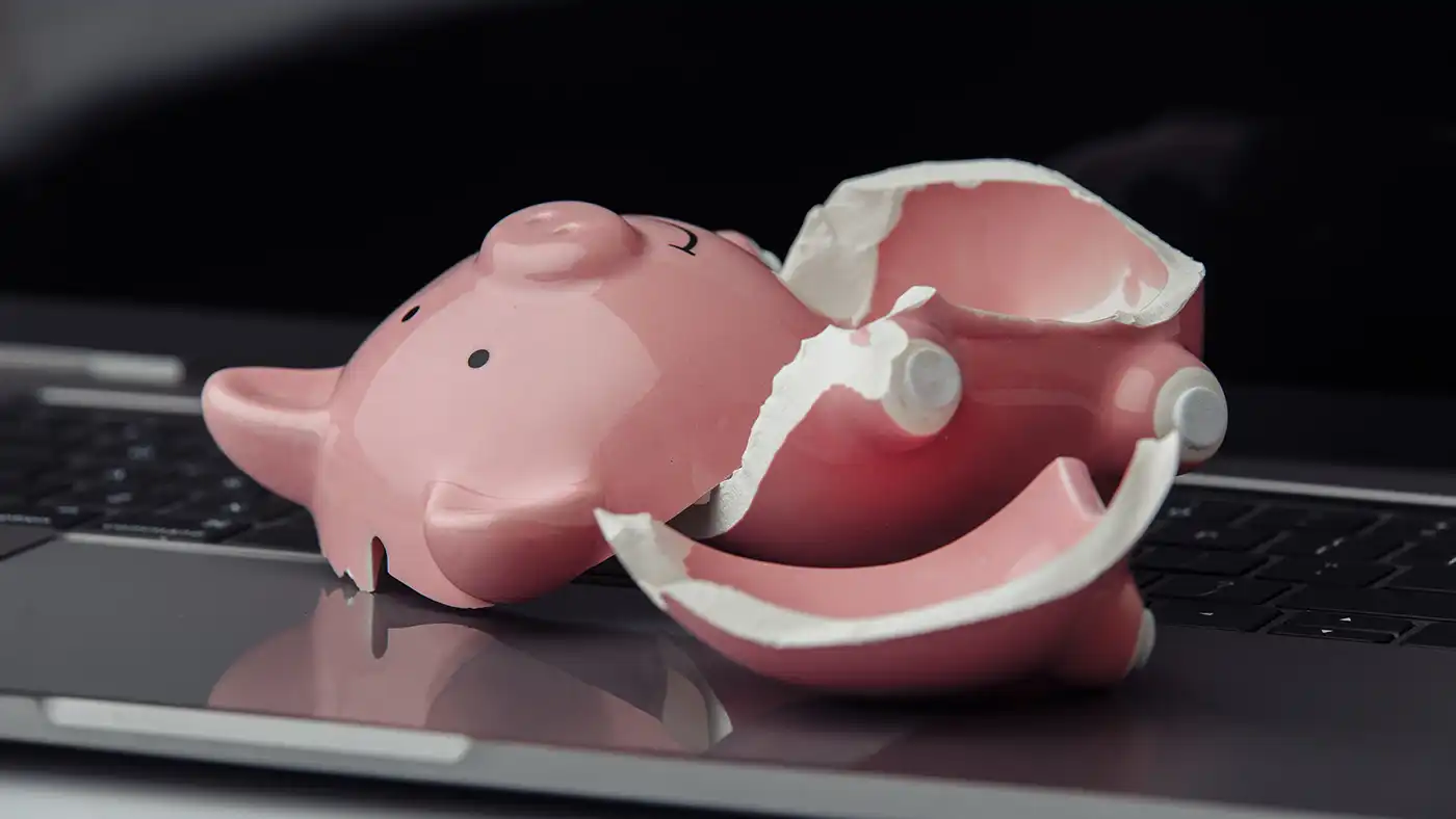 Broken pink piggy bank on top of a laptop close up